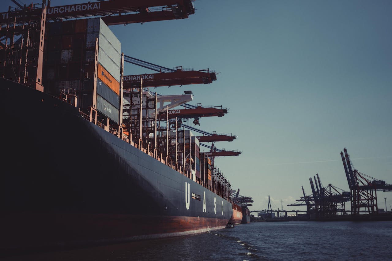Services-02 A large cargo ship docked at Hamburg Harbor, cranes loading containers under a clear sky.